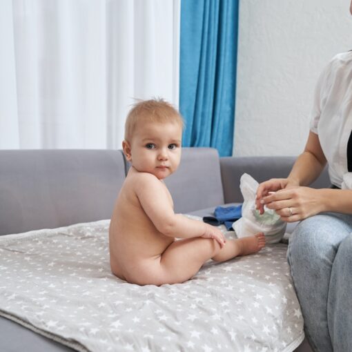 Naked Baby Sitting On Sofa Near Smiling Mother