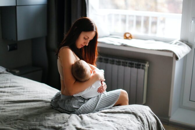 Mother And Baby In The Bedroom On The Bed, Mother Breastfeeds Baby,