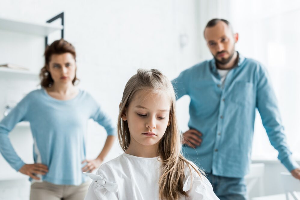 Selective Focus Of Upset Child Near Sad Parents Standing At Home